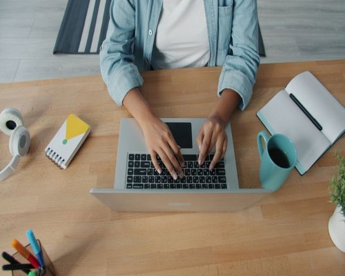 A person typing on a laptop at a neat wooden desk during the morning